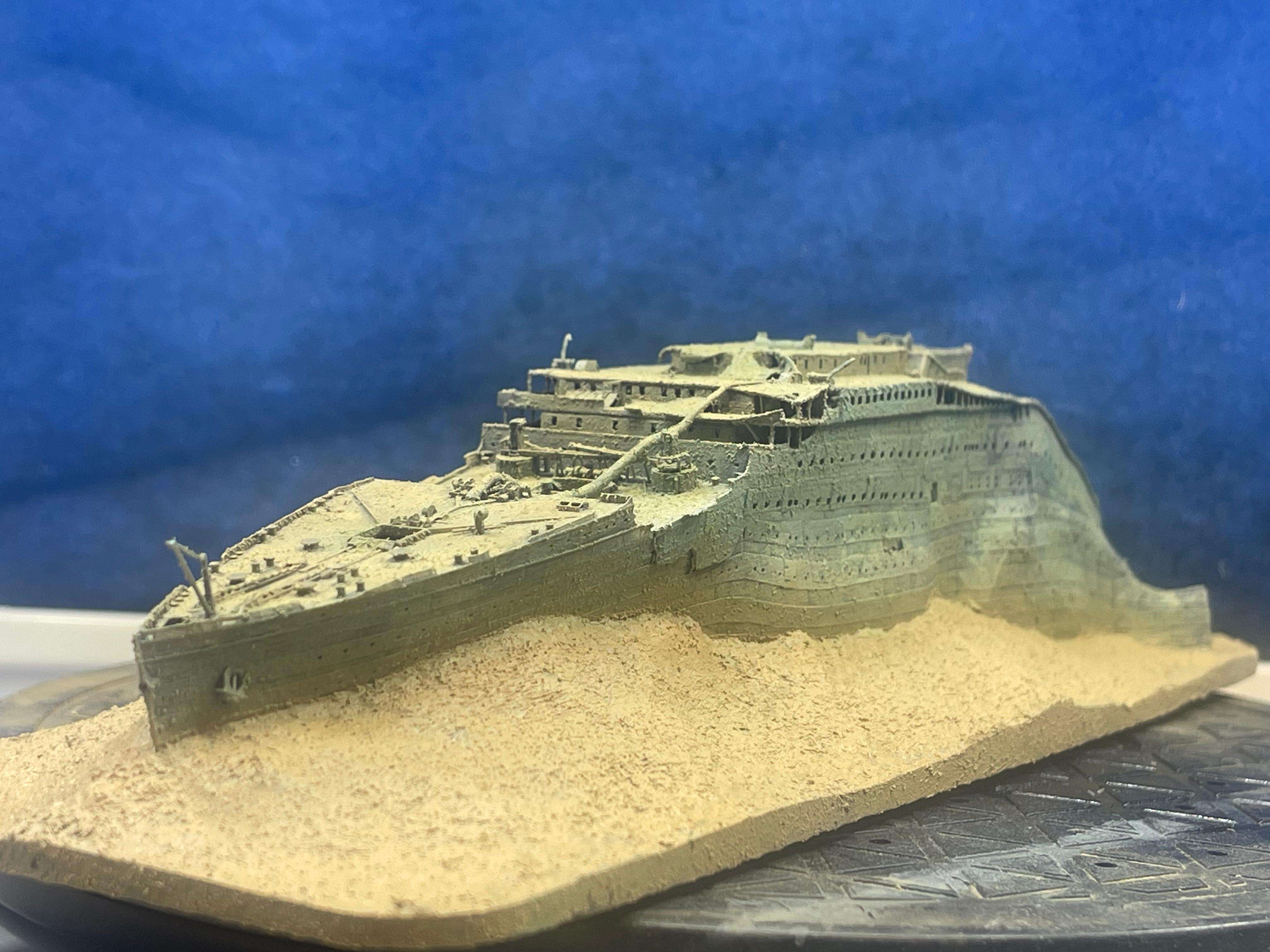 Close-up of a detailed model of the Titanic wreck on a sandy surface